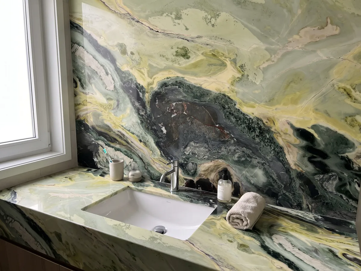 Cubierta de lavabo y pared de baño en mármol verde Dream Green con lavamanos blanco y grifería cromada: ondas verde oscuro y amarillo lima con una zona central muy oscura