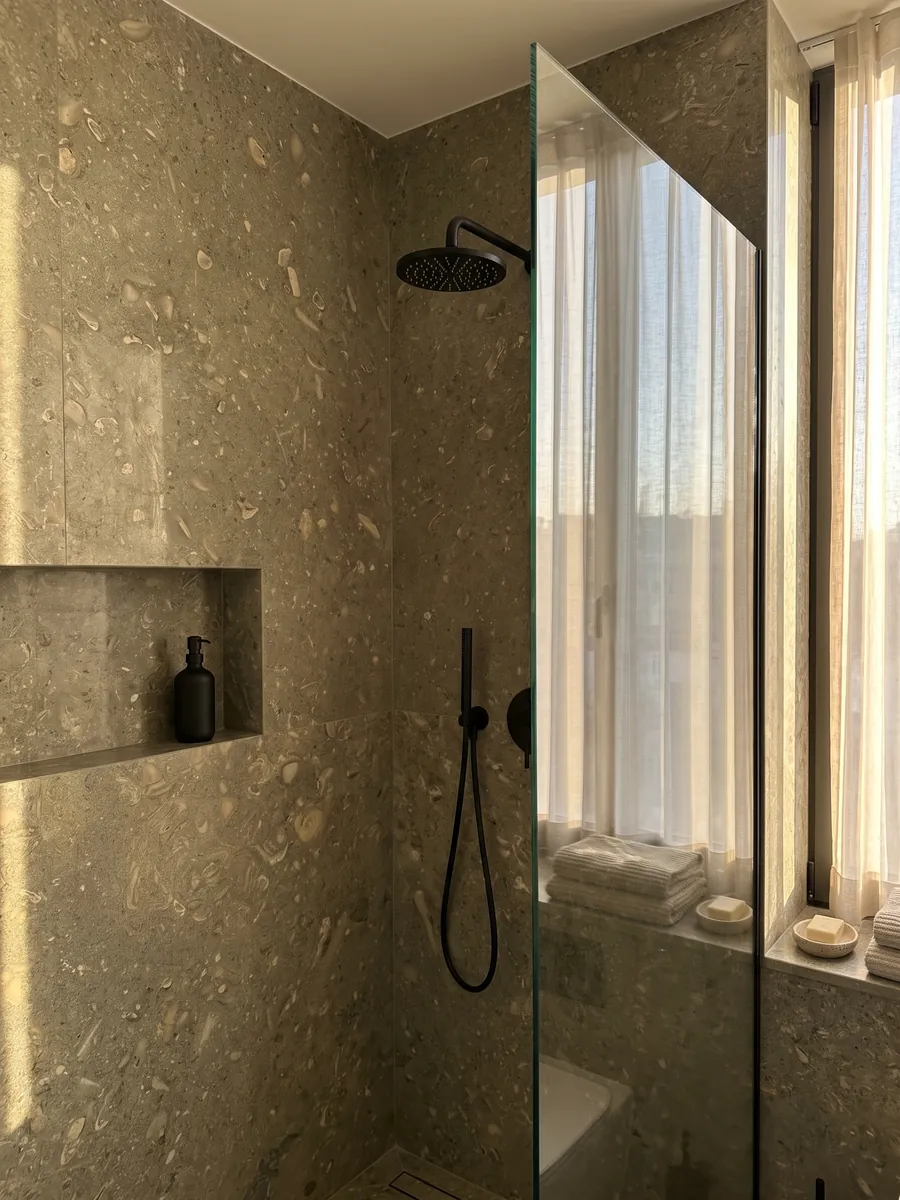 Ducha revestida con placas enteras de mármol verde Fossil Green con nicho empotrado: verde oliva moteado con siluetas de conchas fósiles en tono más claro