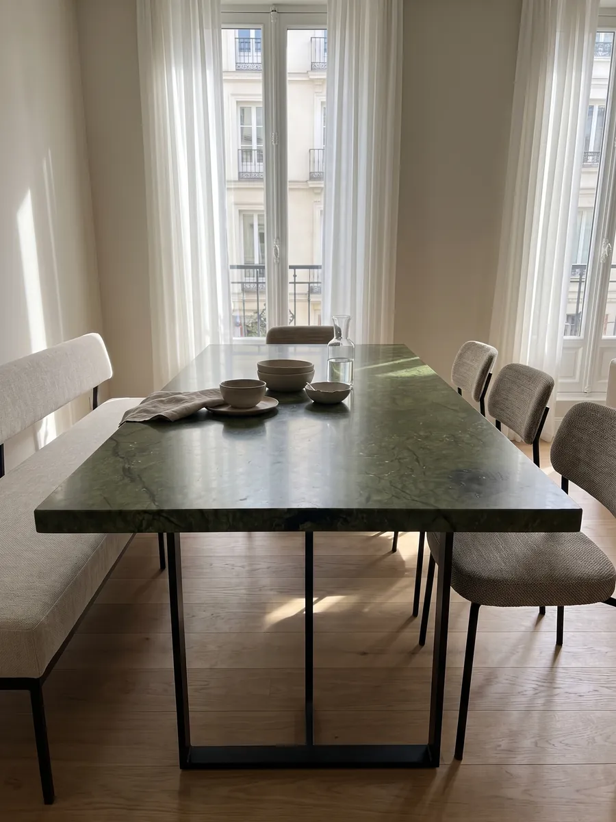 Mesa de comedor con cubierta de Mármol Verde Giada sobre base de acero: verde oliva intenso con nubes de tono y finas grietas oscuras; una mancha oscura abajo a la izquierda