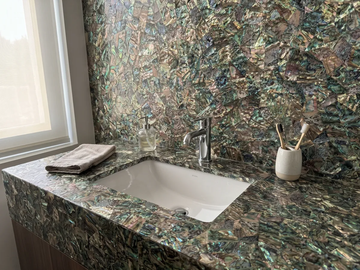 Cubierta de lavabo y pared de baño en Nácar Abulón con lavamanos blanco y grifería cromada: mosaico tupido de concha irisada en verdes, azules y marrones