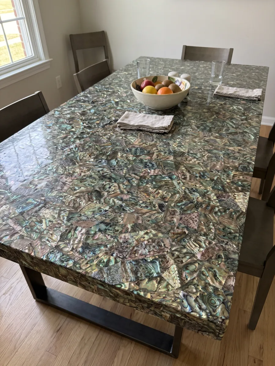 Mesa de comedor con cubierta de Nácar Abulón sobre base de acero: mosaico tupido de concha irisada en verdes, azules y marrones