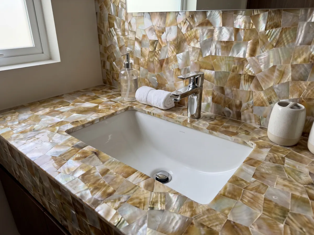 Cubierta de lavabo y pared de baño en Nácar de Concha Dorada con lavamanos blanco y grifería cromada: mosaico de nácar dorado y blanco con reflejos irisados