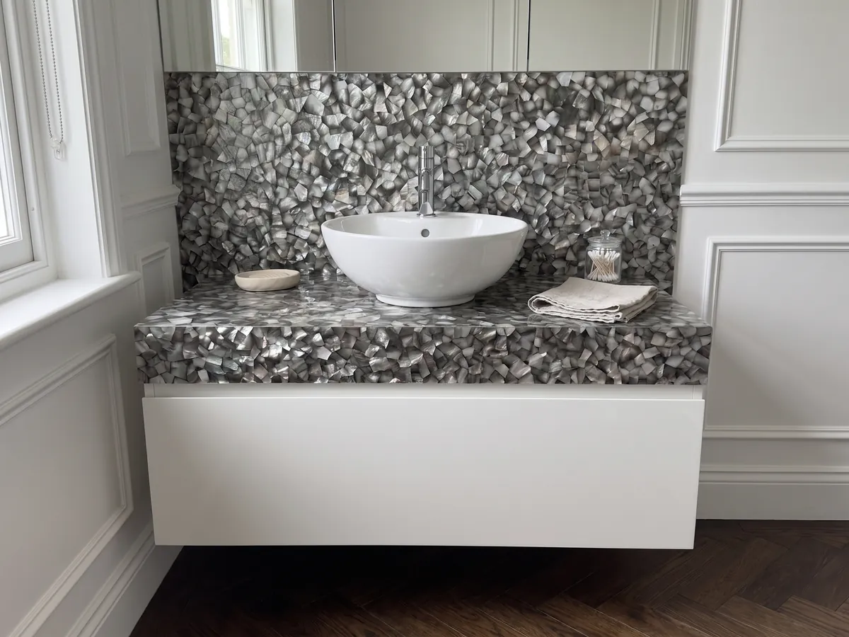 Cubierta de lavabo y pared de baño en Nácar de Concha Gris con lavamanos blanco y grifería cromada: polígonos de nácar gris oscuro y plata con reflejos irisados