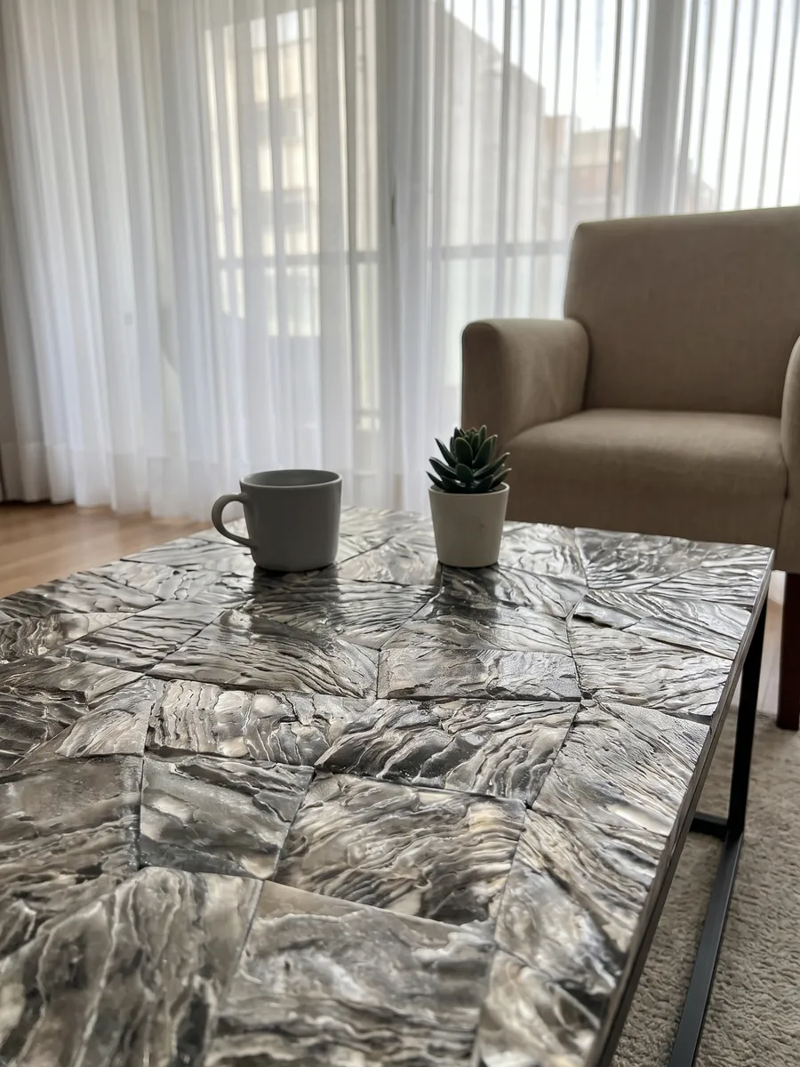 Mesa de centro con cubierta de Nácar Galushell Gris en una sala: piezas de concha gris plata con estrías onduladas de aspecto metálico