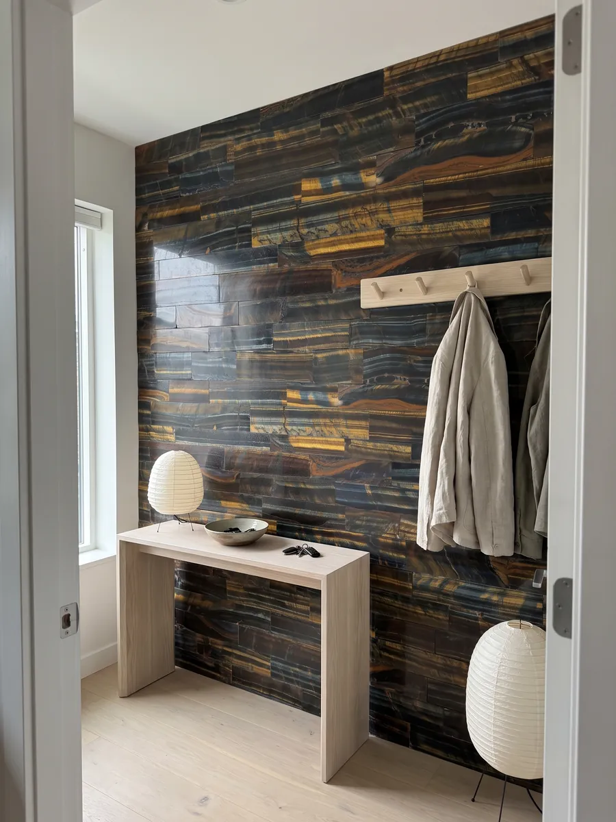 Pared de recibidor revestida con Ojo de Tigre Azul Dorado con consola estrecha: listones horizontales que mezclan azul oscuro con franjas doradas y naranja