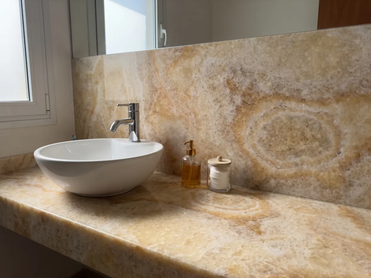 Cubierta de lavabo y pared de baño en Ónix Amarillo con lavamanos blanco y grifería cromada: miel y crema con un anillo ovalado concéntrico bien visible