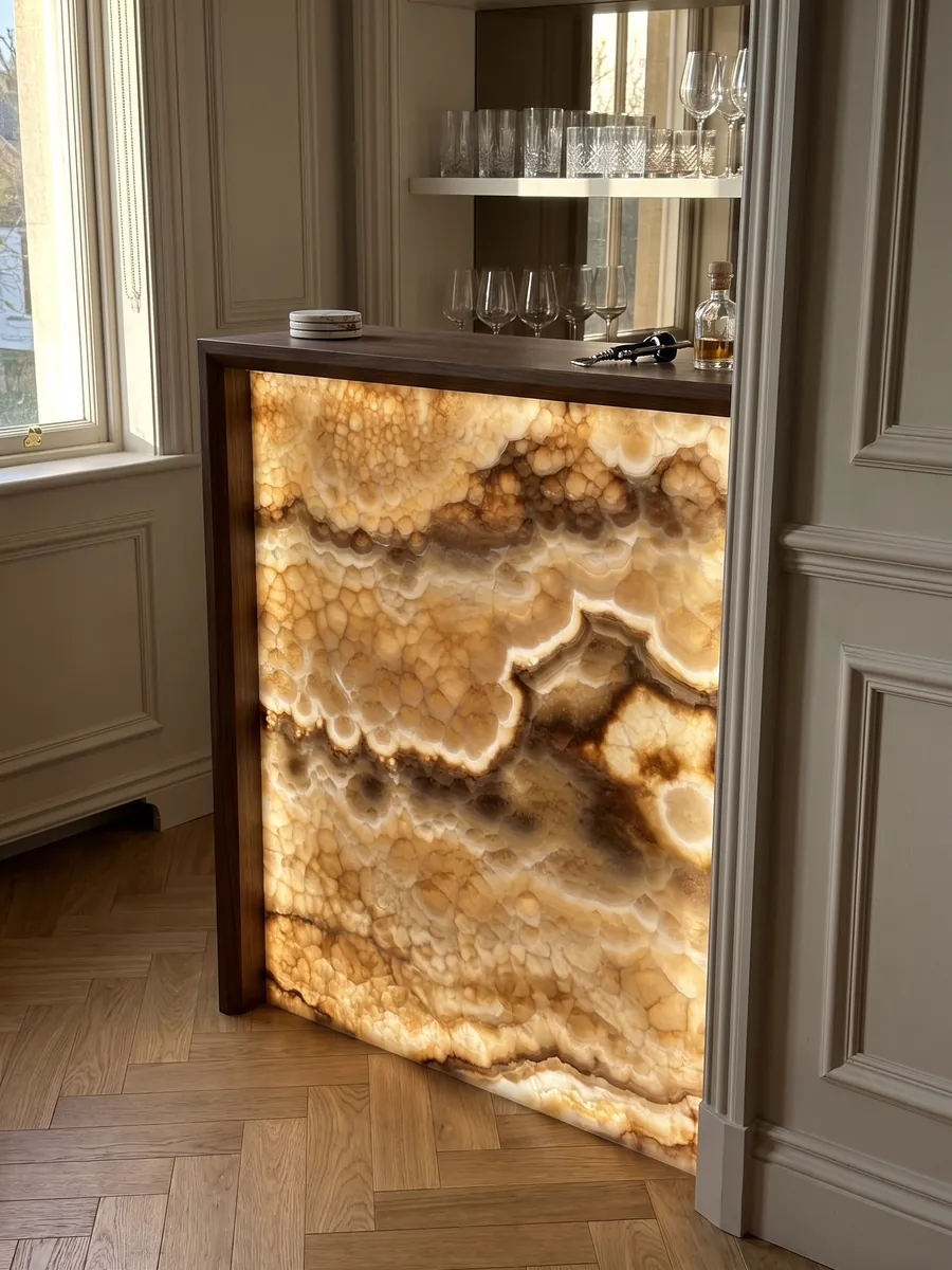 Barra con frente de ónix amarillo Miel Oscuro retroiluminado con la luz atravesando la piedra: ámbar con textura de celdas redondeadas y bandas onduladas marrón oscuro