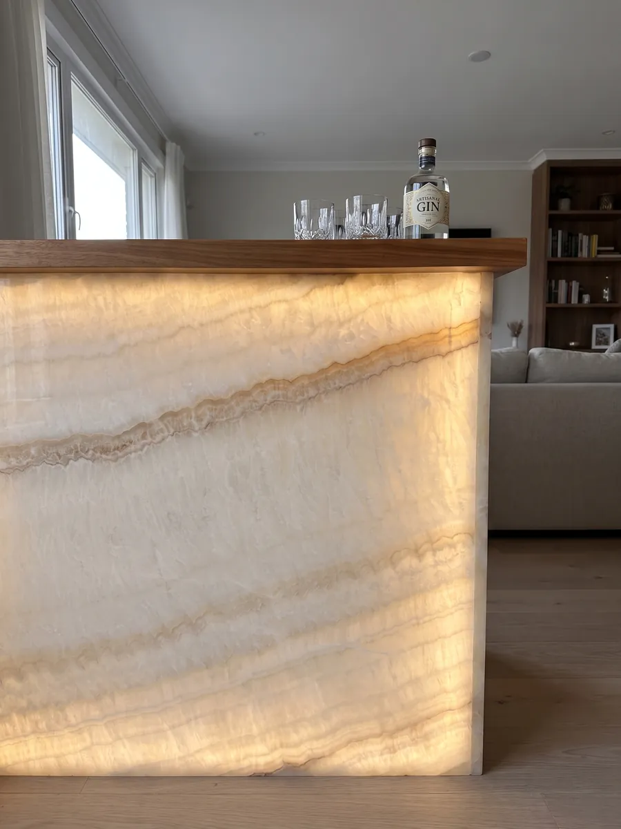 Barra con frente de ónix beige Ivory retroiluminado con la luz atravesando la piedra: marfil suave con ondas tenues y una línea fina color miel en diagonal