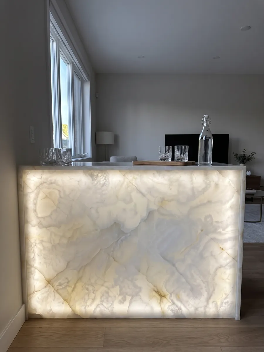 Barra con frente de Ónix Blanco retroiluminado con la luz atravesando la piedra: blanco cremoso traslúcido con nubes suaves y finísimas líneas doradas