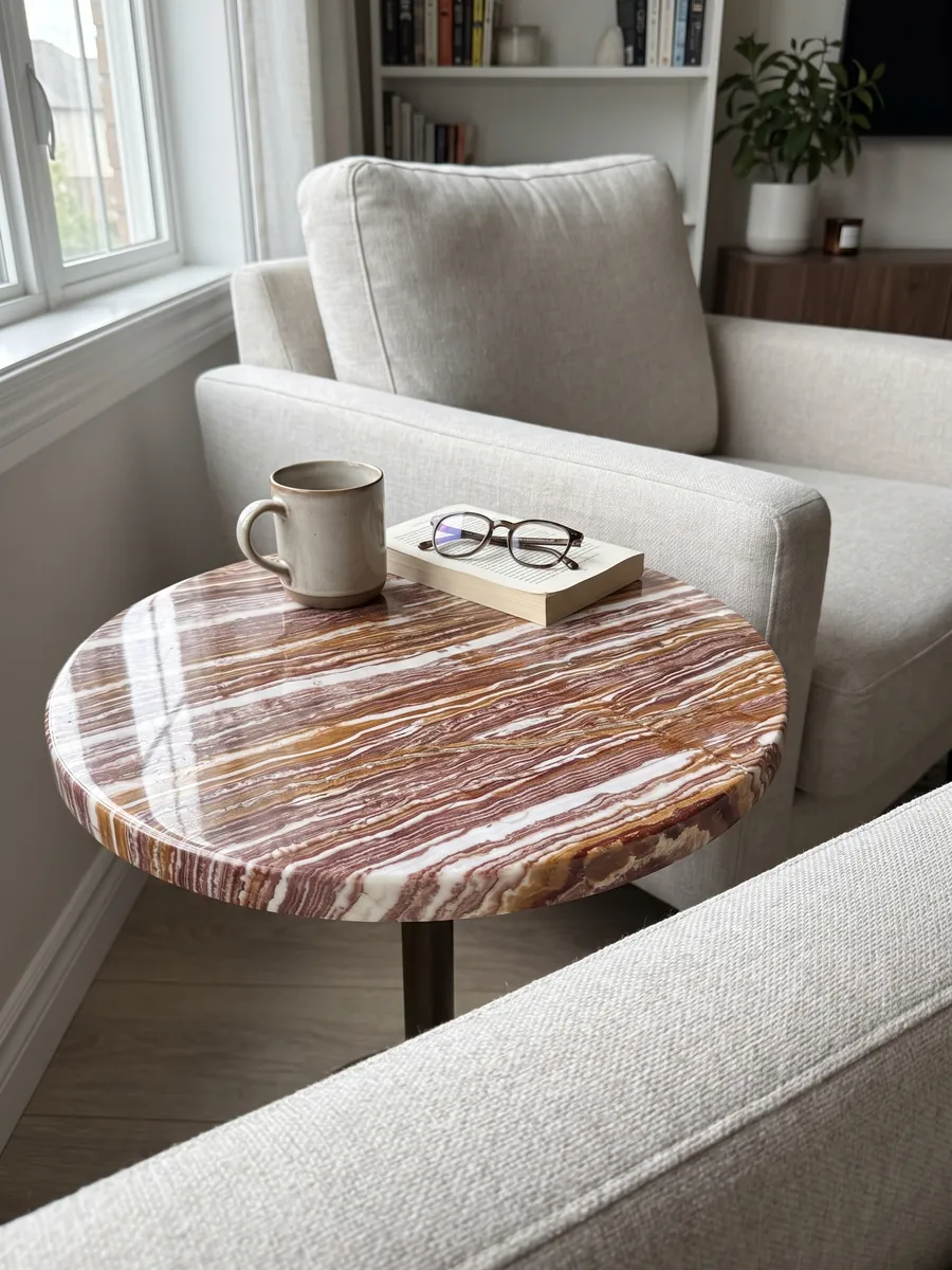 Mesa auxiliar con cubierta de ónix marrón Fantástico junto a un sillón: franjas horizontales alternas blancas, rojizas y ocre, muy marcadas