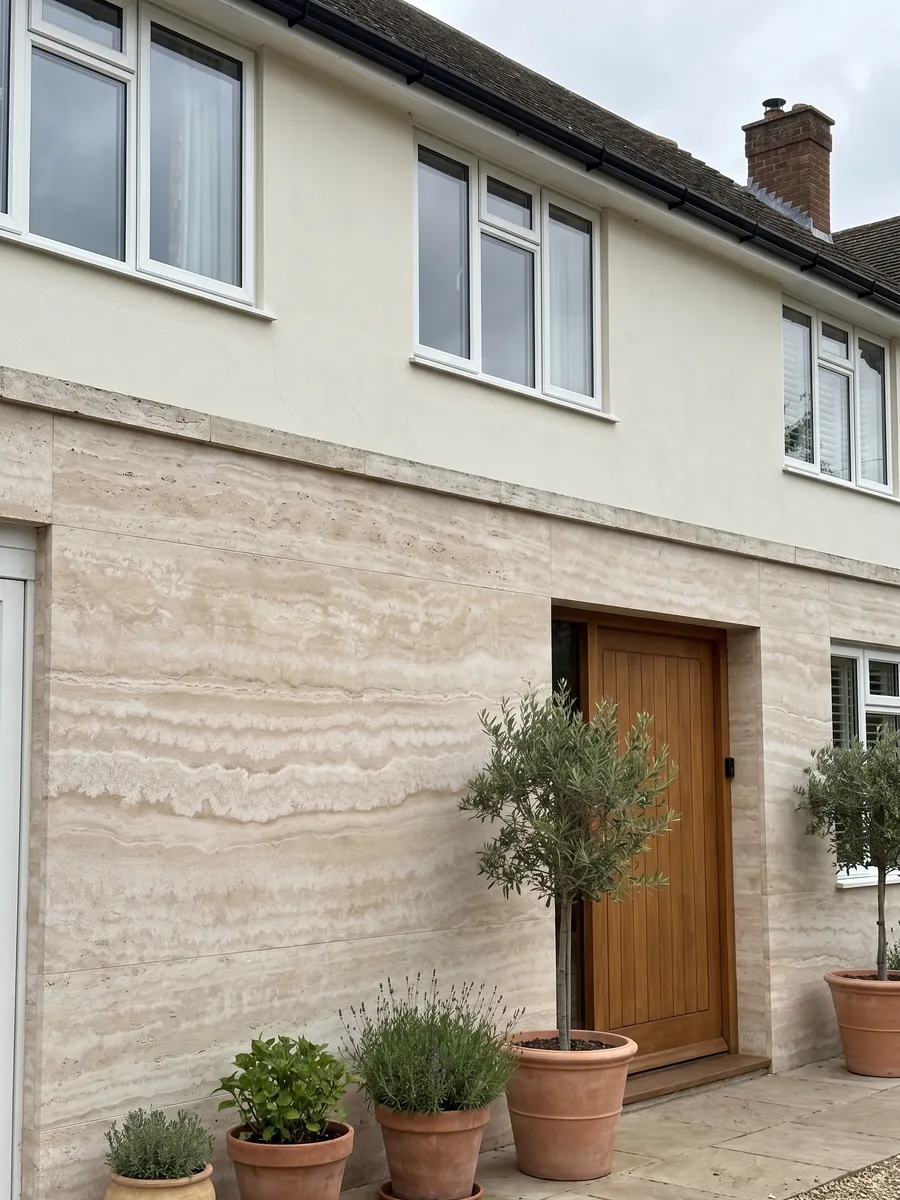 Fachada de casa revestida con travertino beige Paglierino junto a una puerta de madera: crema con bandas horizontales onduladas en tonos muy cercanos