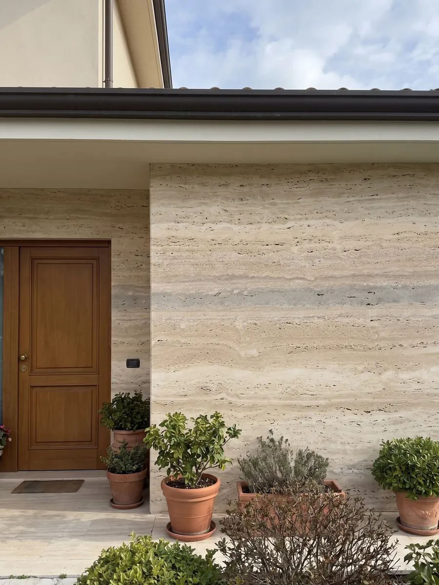Fachada de casa revestida con travertino beige Striato junto a una puerta de madera: beige con franjas horizontales finas y alguna banda gris más ancha