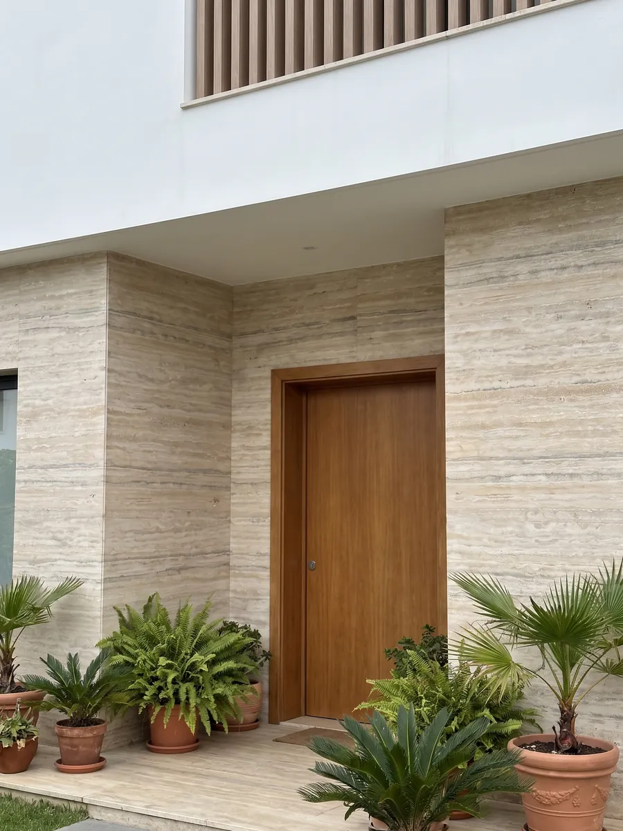 Fachada de casa revestida con travertino gris Ocean Silver junto a una puerta de madera: franjas horizontales finas beige y grises con algunos poros