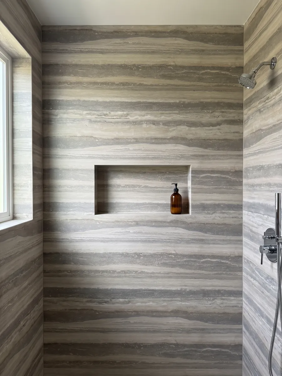 Ducha revestida con placas enteras de travertino gris Silver con nicho empotrado: franjas horizontales anchas gris y beige claro, ordenadas y paralelas