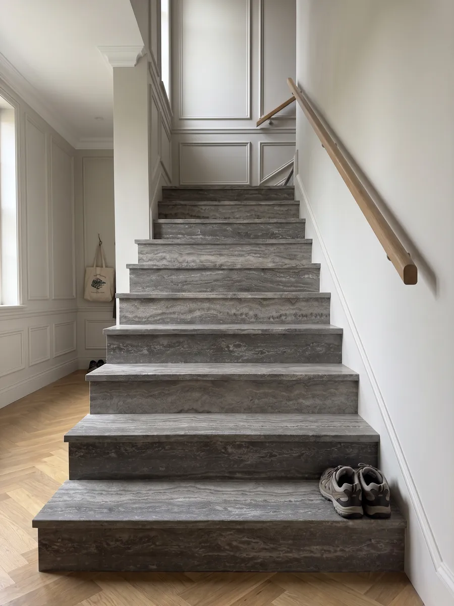 Escalera interior con peldaños de travertino gris Titanium con pasamanos: gris con bandas horizontales onduladas que pasan de claro a oscuro