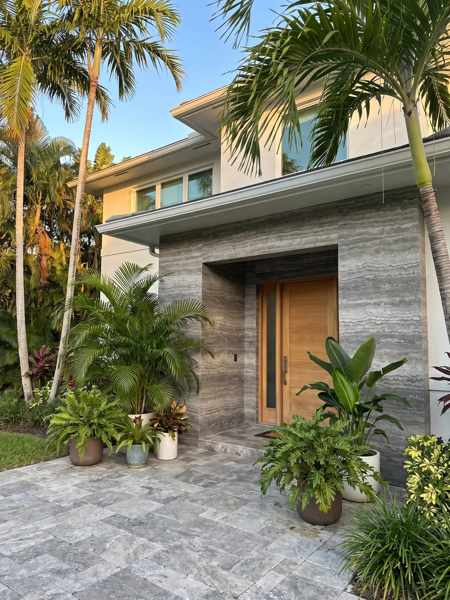 Fachada de casa revestida con travertino gris Titanium junto a una puerta de madera: gris con bandas horizontales onduladas que pasan de claro a oscuro