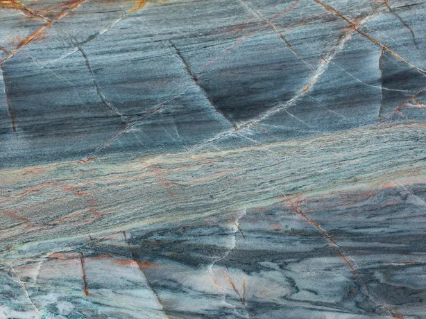 Detalle de la cuarcita azul Blue Atlantic: líneas naranja ocre y vetas blancas cruzadas en ángulo sobre el pulido brillante