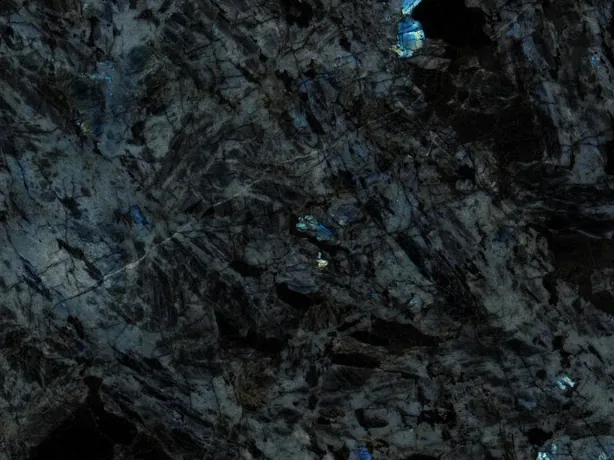 Detalle de la cuarcita negra Lemurian: cristales alargados oscuros y destellos azul eléctrico sobre el pulido