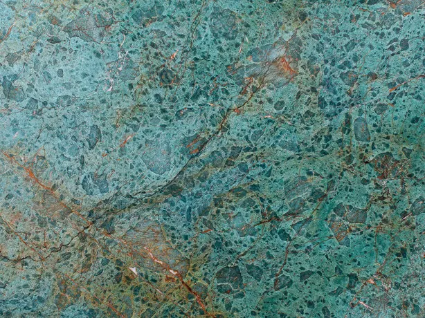Detalle de la cuarcita verde Tanzanite: granos turquesa y la banda rojo óxido sobre el fondo verde azulado