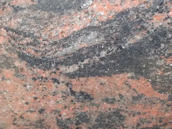 Placa de Granito Indian Aurora: bandas onduladas de coral, gris y negro en diagonal sobre fondo gris oscuro
