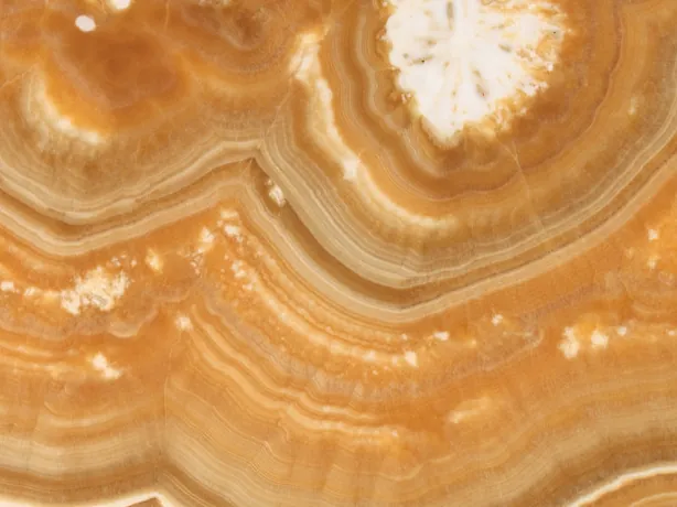 Detalle del Ónix Arancio: la curva de bandas naranja, ámbar y crema con el brillo del pulido