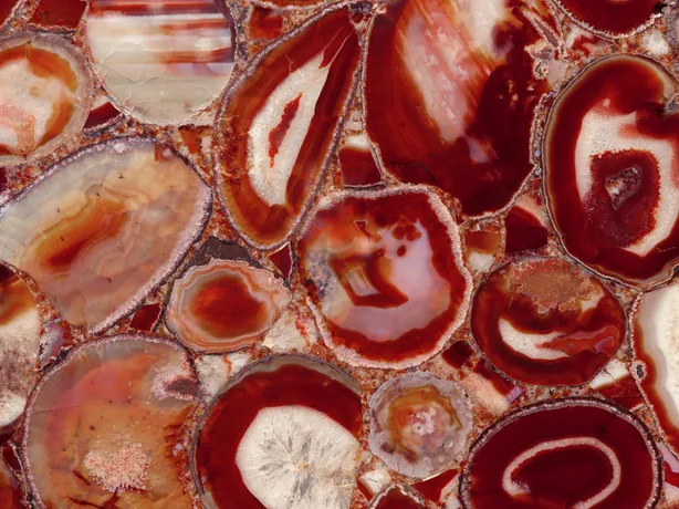 Detalle del Ágata Roja: anillos rojos alrededor de centros crema sobre fondo burdeos, con brillo de pulido