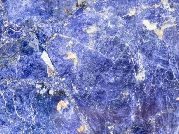 Detalle de la sodalita: vetas blancas irregulares y pequeñas motas naranjas sobre el azul violeta