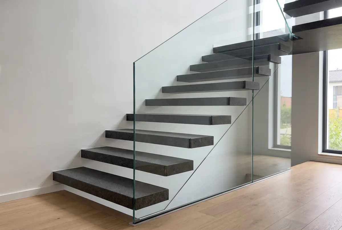 Escalera con huellas voladas de granito gris oscuro y baranda de vidrio