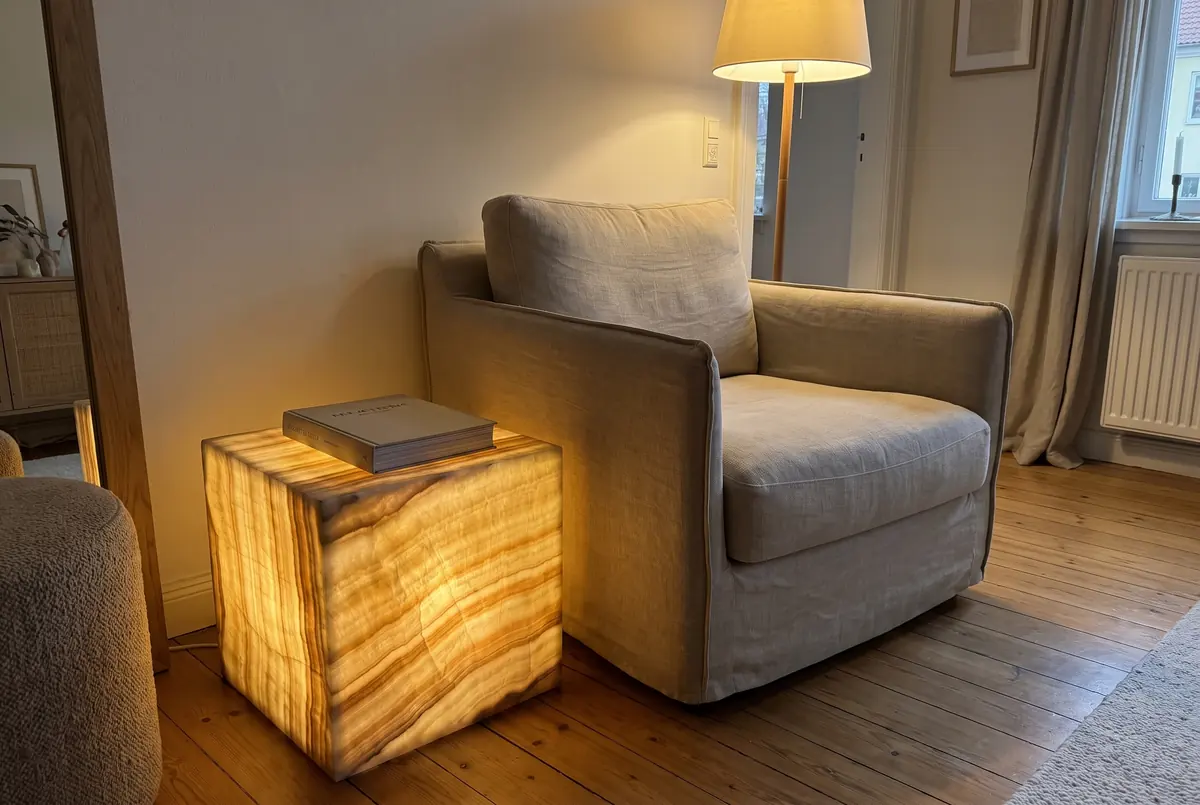 Mesa auxiliar en forma de cubo de ónix color miel iluminada desde dentro, junto a un sillón