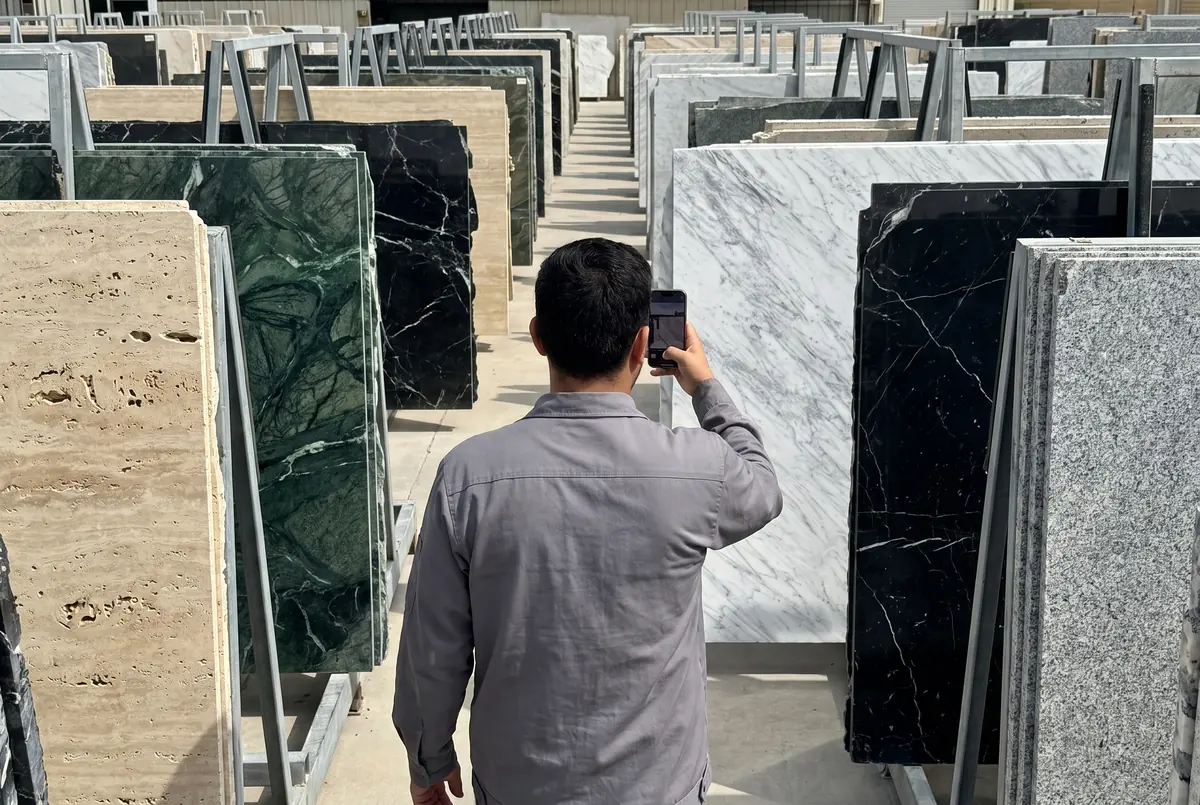 Una persona recorre un patio de placas de piedra natural y fotografía una placa de mármol blanco